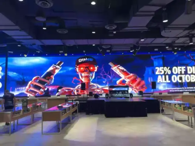 Planet 13 store interior with a large LED wall looping a Dime Industries promotion, 25% off all October, above a stage and product counters